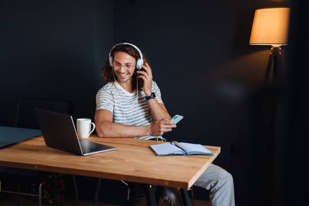 istock Young man using laptop and headphones while sitting by desk in office 1463386005