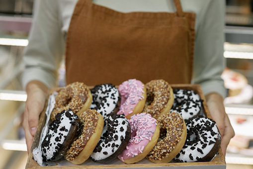 Tray with various fresh delicious donuts in hands of bakery owner