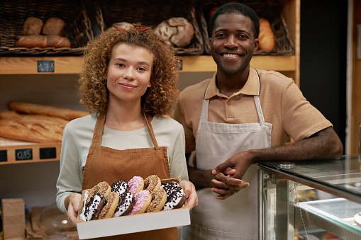 Portrait of happy bakery owners with box of fresh donuts