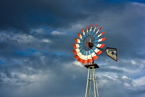 Red, white and blue well pumping, farming windmill with dramatic sky.