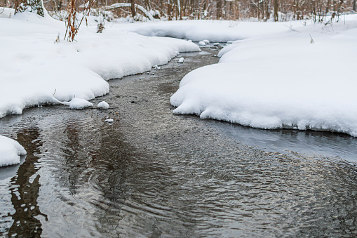 Winter landscape with an unstoppable stream of water (stream) surrounded by white snows.