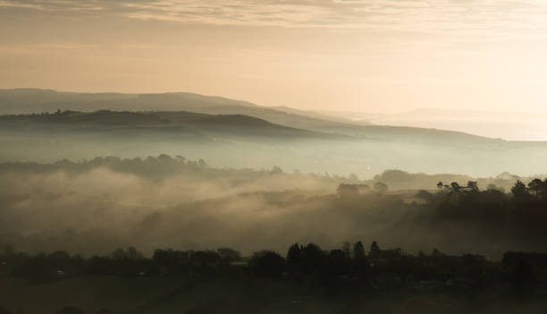istock Ethereal shot of a field with hills covered in trees under clouds during sunset 1463387996