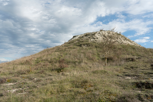 A low angle shot of a hill covered in dried grass under the cloudy sky