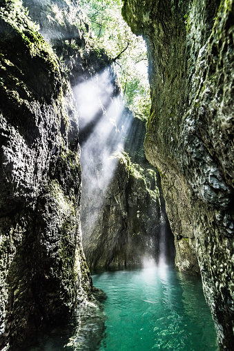 A vertical shot of the sunlight coming into a water cave from between the rocks