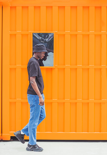 A vertical shot of a young afro-American man posing in front of an orange background in France