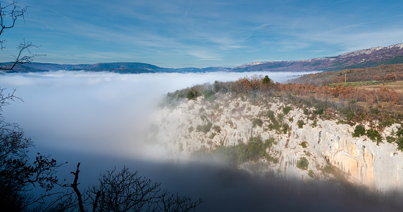 A scenic view of a sea of clouds beside a mountain cliff with autumn trees