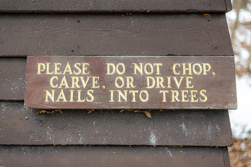 Weathered wood sign on building, please do not chop, carve, or drive nails into trees.
