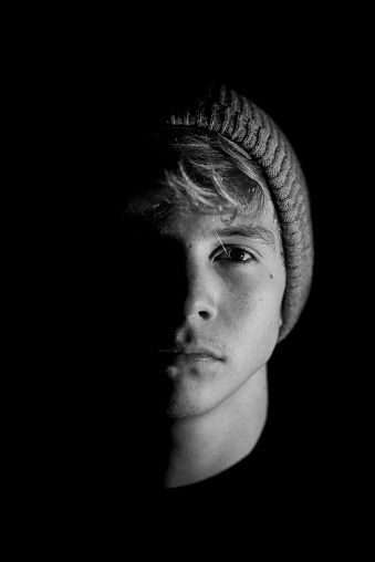 A vertical grayscale portrait of a young Caucasian man half of the face in the shadow.