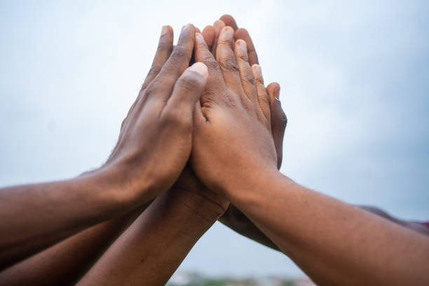 istock Hands of African people doing group high-five with a light blue sky on the background 1463402964