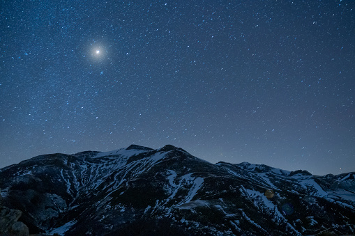 A scenic view of a slope of a snowy mountain under the starry night sky