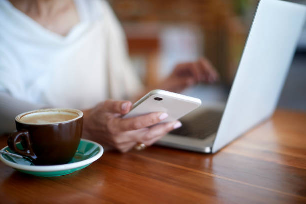 istock Hand, phone and coffee with a woman customer using a laptop in a cafe while typing a text message. Mobile, computer and social media with a female patron sitting alone at a table in a restaurant 1463407129