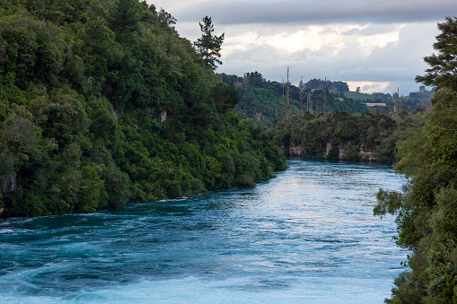 A landscape shot of a flowing river in Taupo in the north island of New Zealand. The river is turquoise in colour and the river banks are rich in foliage.