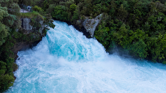 A vibrant shot taken looking down onto Huka Falls in Taupo in the north island of New Zealand. The water is turquoise in colour with thick green foliage on the cliff and rock face.