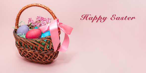 Colorful Easter eggs in wicker basket on pink background.