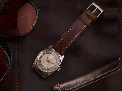 Classic vintage wristwatch with brown leather strap and a wallet and sunglasses