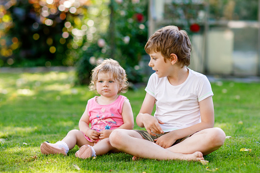 Happy little kid boy with cute little baby girl, cute sister. Siblings. Brother and baby playing together in summer garden with flowers. Family and love.