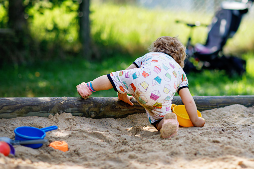 Cute toddler girl playing in sand on outdoor playground. Beautiful baby in summer clothes having fun on sunny warm summer day. Outdoors activity for toddlers