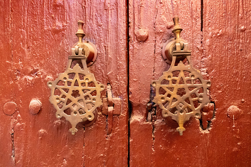 Close-up of a red-brown wooden door with two Arab-style metal knockers. The photo was taken in the medina of Marrakech, Morocco