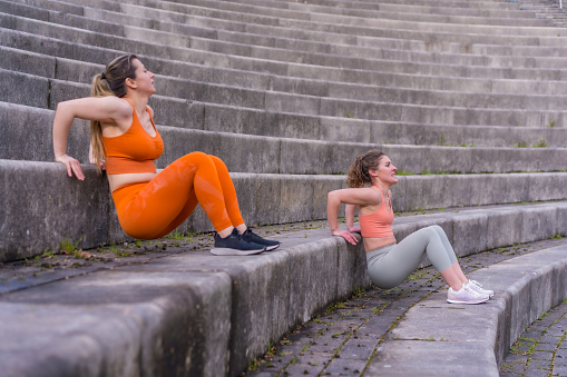 Two young fitness girls in a city park, dippings on the steps