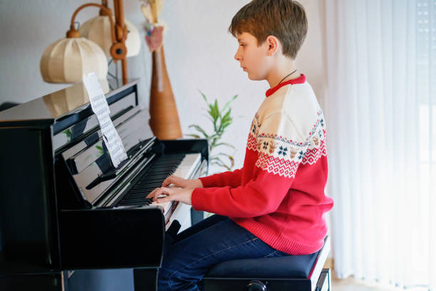 schuljunge spielt klavier im wohnzimmer. kind hat spaß beim erlernen des musikinstruments. talentiertes kind zu hause. - romrodinka stock-fotos und bilder