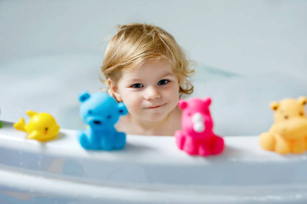 adorable cute little toddler girl taking bath in bathtub. happy healthy baby child playing with rubber gum toys and having fun. washing, cleaning, hygiene for children. - bath toy imagens e fotografias de stock