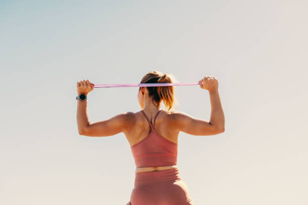 Female in her 30s is embracing her active lifestyle. She is outdoors, wearing sportswear and exercising with an exercise band. She has a keen interest in physical fitness and is stretching and working out in the bright sunlight. This woman is demonstrating her commitment to wellness and wellbeing, as she pursues a healthy and fit lifestyle.