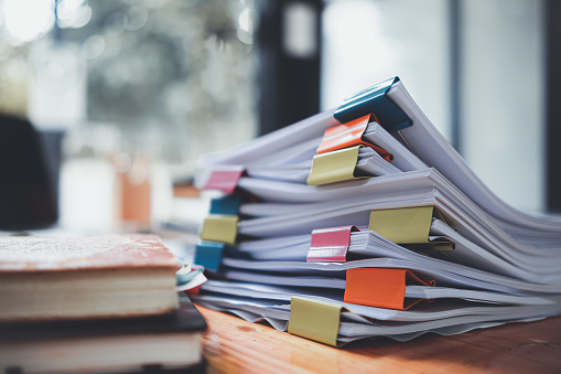 The stacks of documents lying on the desk are waiting to be verified before being sent to the Board of Directors to use the correct information before meeting with businessmen and investors.