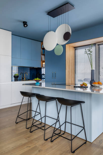 istock Interior design of kitchen interior with marble kitchen island, blue wall, black chokers, bowl with fruits, big window, cup, wooden floor, lamp on wall and personal accessories. Home decor. Template. 1463435036