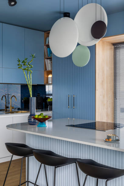 istock Interior design of kitchen interior with marble kitchen island, blue wall, black chokers, bowl with fruits, big window, cup, wooden floor, lamp on wall and personal accessories. Home decor. Template. 1463435136