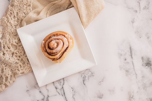 Cinnamon roll on white plate, marble top