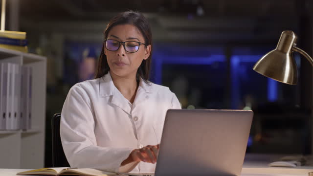 Doctor, notebook or scientist woman with laptop for medical research or healthcare data analysis review at night. Nurse, book or professional girl in lab on tech for medicine, wellness or note study