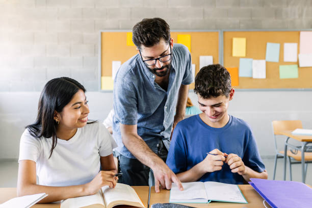 Male teacher helping high school students doing exercises in classroom stock photo