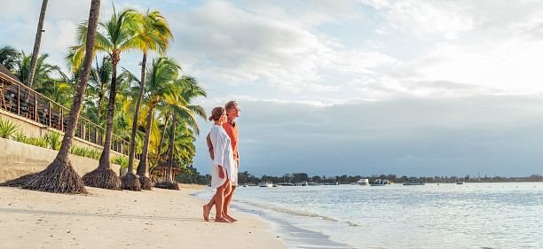 Pareja enamorada abrazándose en una playa exótica de arena mientras pasea por la costa de Trou-aux-Biches en la isla de Mauricio disfrutando de la puesta de sol. Relación con las personas y vacaciones de luna de miel tropicales imagen conceptual photo