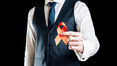 Aids awareness. Red ribbon symbol in hiv world day in man hand isolated on dark background. Awareness aids and cancer. Healthcare and medical concept.