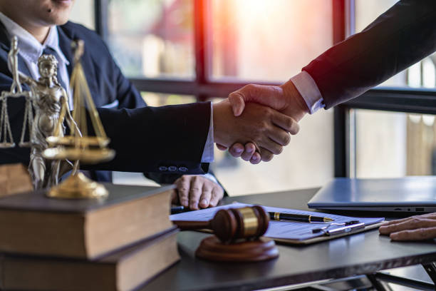 Lawyer shaking hands with client after deal, making deal, signing contract. Law firm, brass scale and hammer, legal and justice consulting services in law office. stock photo