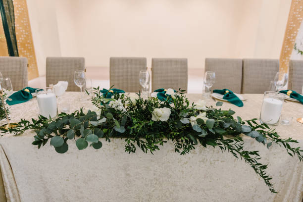 istock Wedding set up, dinner table reception. Flower composition with eucalyptus leaves and candles in the center of the table. A plate with a green cloth towel, knives and forks next to the plate.  Closeup 1463458447
