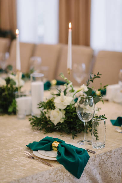 istock Wedding set up, dinner table reception. A plate with a green cloth towel, knives and forks next to the plate. Flower composition with eucalyptus leaves in the center of the table and burning candles. 1463458480