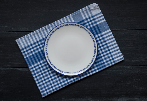 Top view of blank white dish and blue tablecloth on a wood background