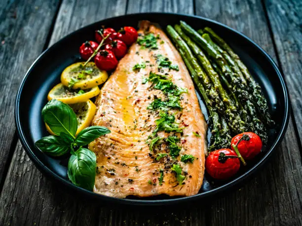 Photo of Fried salmon fillet, asparagus and fried tomatoes on wooden background