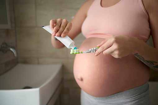 Pregnant, woman and closeup while brushing teeth for oral hygiene, product and toothbrush in a bathroom. Pregnancy, zoom and hands with toothpaste, female and grooming, cleaning and teeth whitening