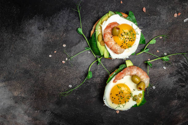 istock Two toasts with wholemeal bread, egg, spinach, avocado, shrimps on dark background, Ketogenic breakfast. superfood concept. Healthy, clean eating. Top view 1463463179