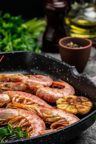 Photo of Grilled tiger shrimps with spice, lemon and garlic in a frying pan on a dark background. Prawns fried on a dark background, Seafood appetizer, Culinary, cooking concept, top view