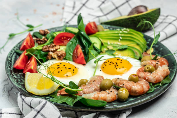 istock Ketogenic diet breakfast shrimps, prawns, soft fried egg, fresh salad, tomatoes, cucumbers and avocado on a dark background. Keto, paleo lunch. Top view 1463463287