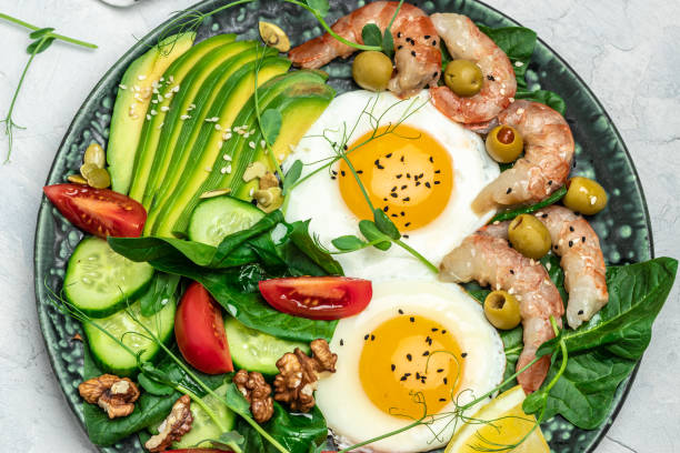 istock Ketogenic diet breakfast shrimps, prawns, soft fried egg, fresh salad, tomatoes, cucumbers and avocado on a dark background. Keto, paleo lunch. Top view 1463463304
