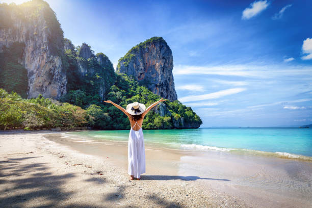 una donna turista felice in un vestito bianco e si trova sulla bellissima spiaggia di railay - mountain looking at view beach cliff foto e immagini stock