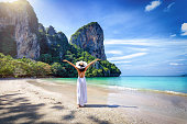 A happy tourist woman in a white dress and stands on the beautiful beach of Railay
