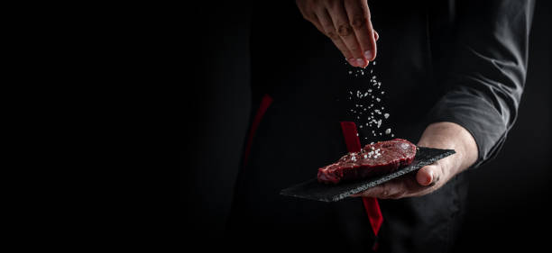 Chef hands cooking meat steak and adding seasoning in a freeze motion. Fresh raw Prime Black Angus beef rump steak. banner, menu recipe stock photo