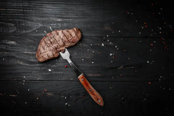 Rump Steak on fork on dark wooden background. banner, menu recipe place for text, top view.