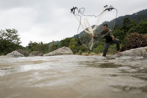 A Japanese man getting set up to do Fly fishing at a rocky creek in the mountains.
