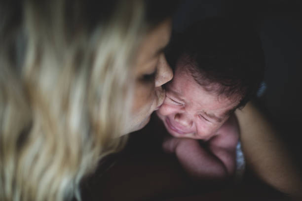 Close-up of a newborn baby girl held by her mother crying.